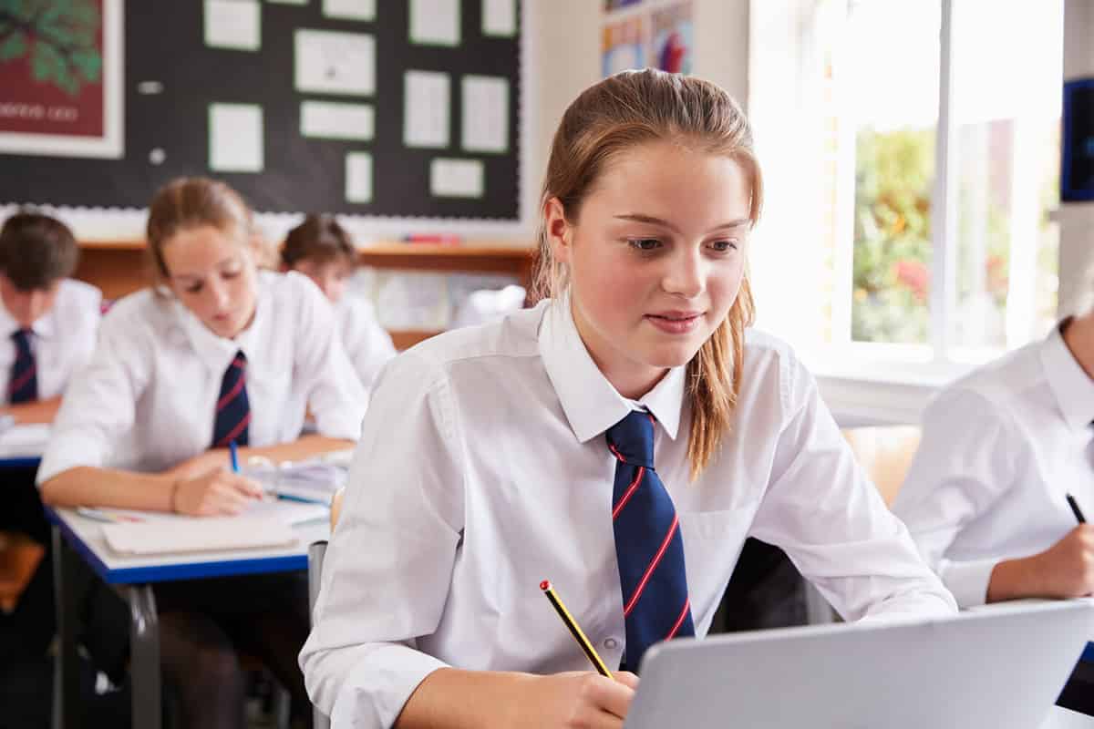 Female Pupil Wearing Uniform Using Laptop In Classroom