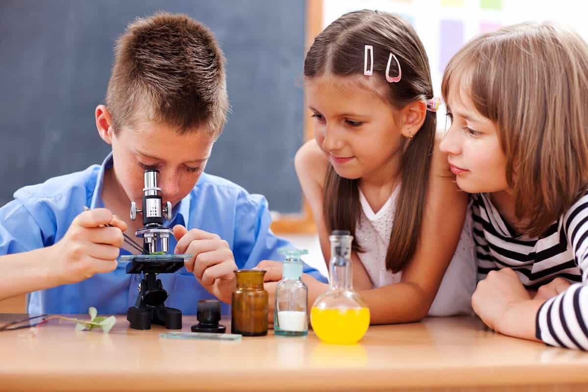 Eminent elementary school boy looking into microscope while girls are watching