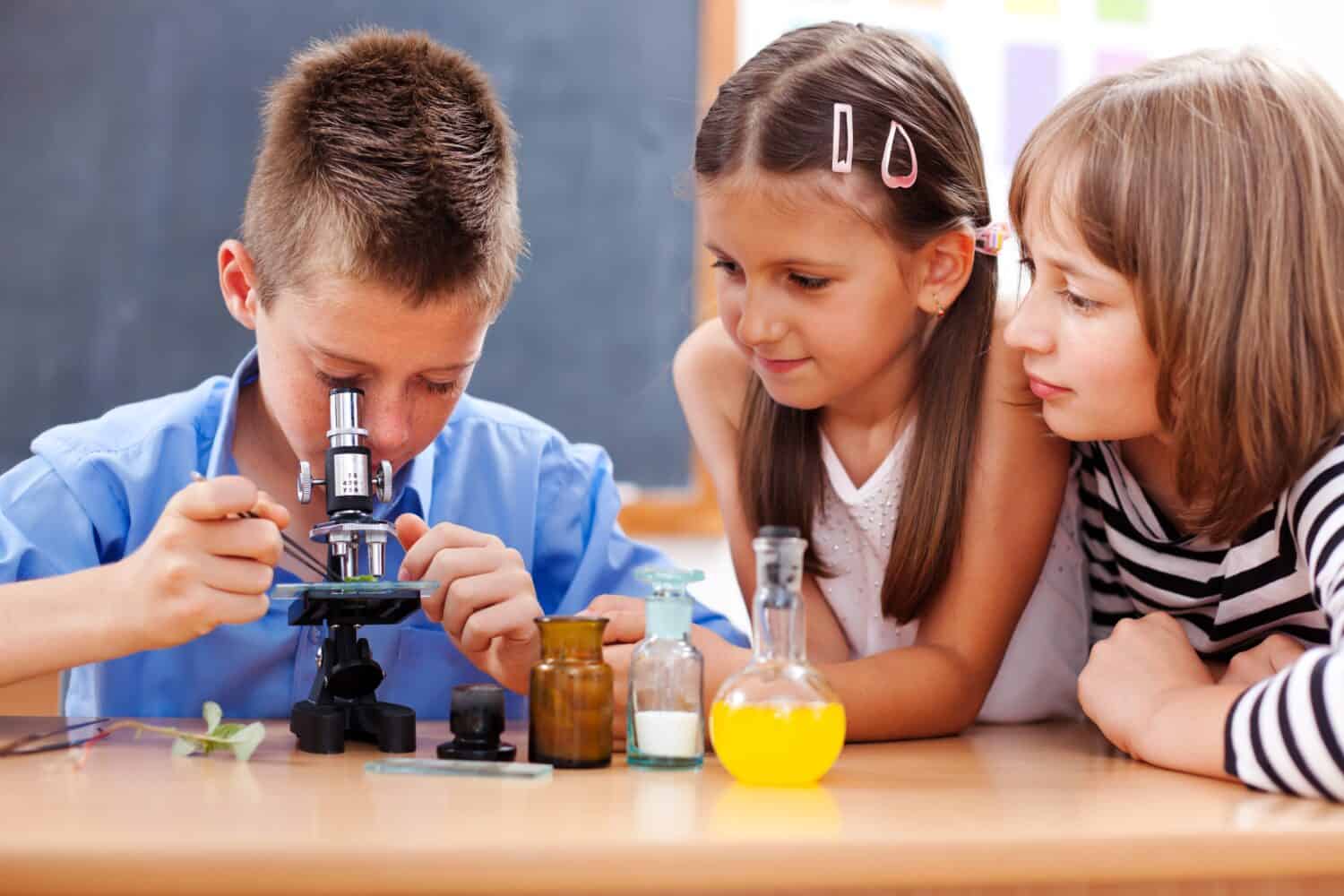 Eminent elementary school boy looking into microscope while girls are watching