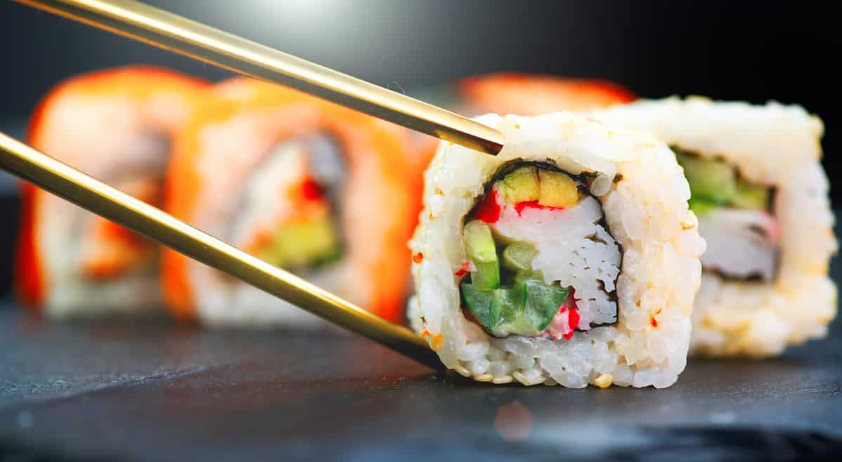 Eating Sushi with chopsticks. Sushi roll japanese food in restaurant. California Sushi roll set with salmon, vegetables, flying fish roe and caviar closeup. Japan restaurant menu