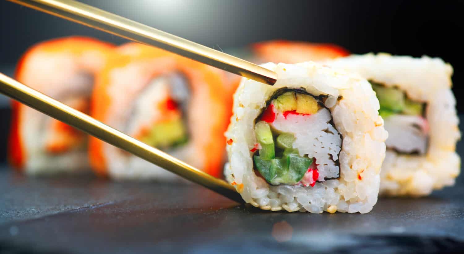 Eating Sushi with chopsticks. Sushi roll japanese food in restaurant. California Sushi roll set with salmon, vegetables, flying fish roe and caviar closeup. Japan restaurant menu