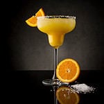 Orange margarita cocktail with tequila, triple sec, orange juice, crushed ice and some salt on the rim of a glass, decorated with a slice of orange