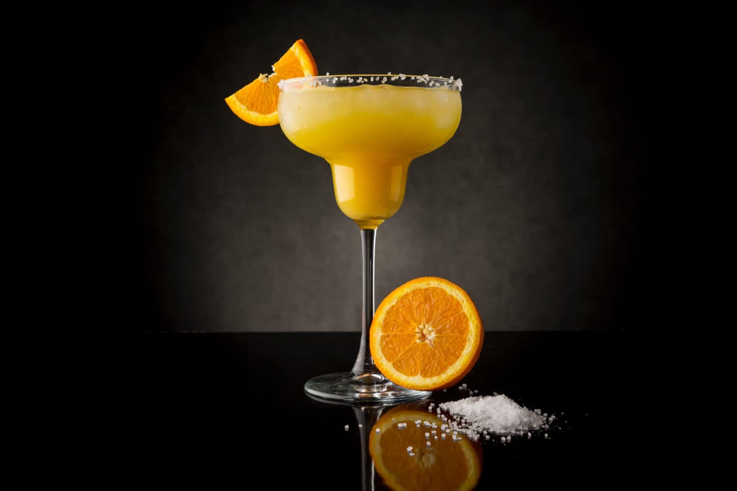 Orange margarita cocktail with tequila, triple sec, orange juice, crushed ice and some salt on the rim of a glass, decorated with a slice of orange