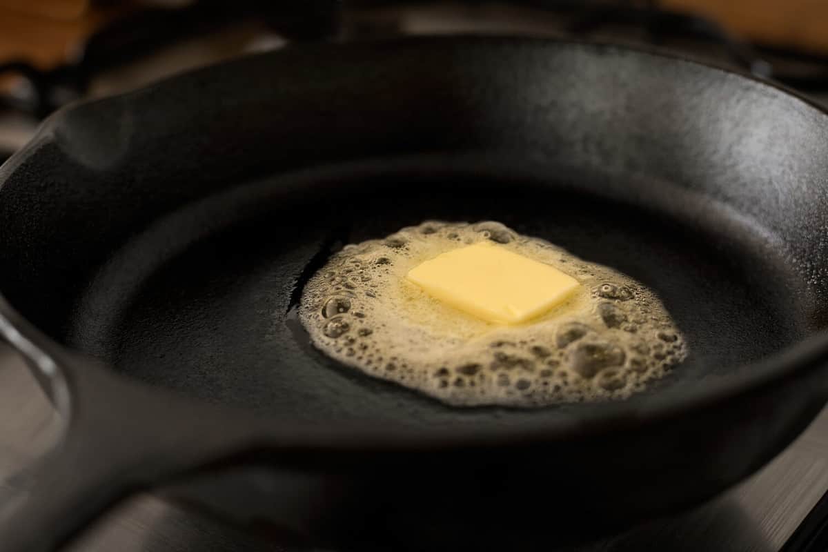 A butter pat melting on a black cast iron frying pan.