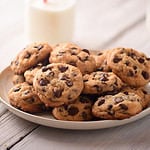 Pile of Delicious Chocolate Chip Cookies on a White Plate with Milk Bottles