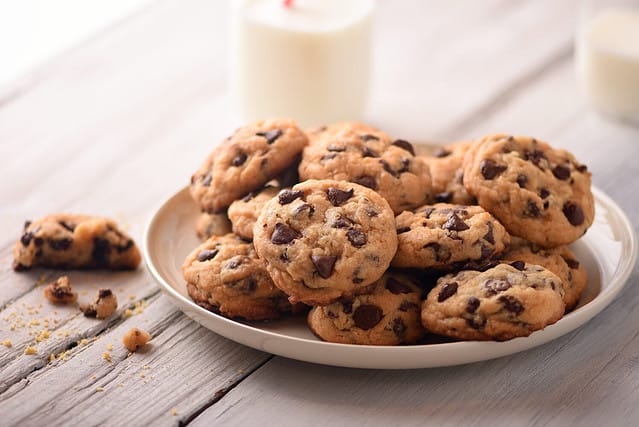 Pile of Delicious Chocolate Chip Cookies on a White Plate with Milk Bottles
