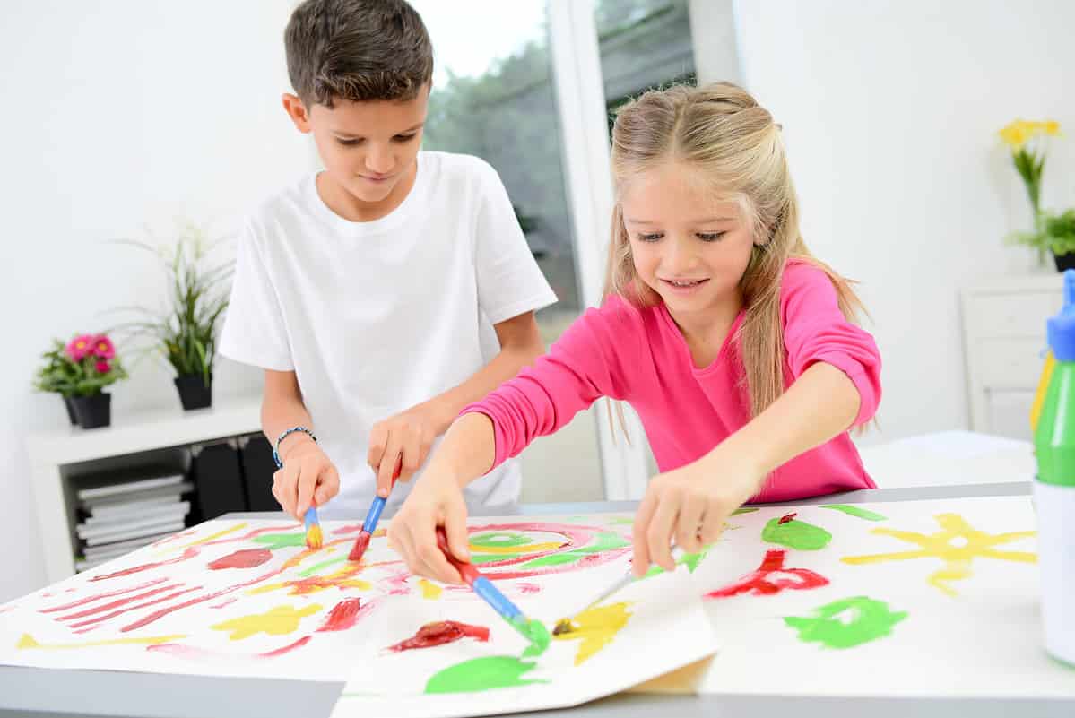 two beautiful young kids boy and girl hand painting on a white paper with color paint
