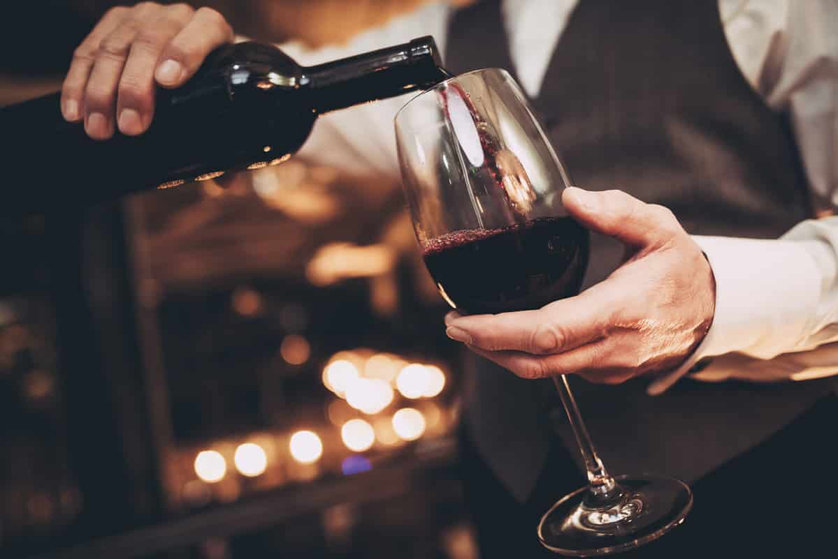 Close up. Elegant waiter pours red wine from bottle into glass at restaurant. Sommelier tasting wine in restaurant.