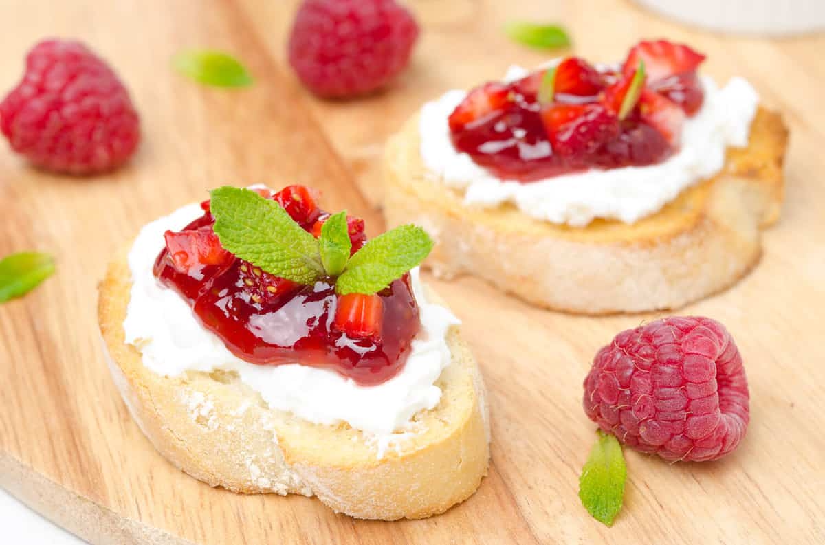 Toasted baguette with cream cheese, raspberry jam, raspberry and mint on a wooden board close-up