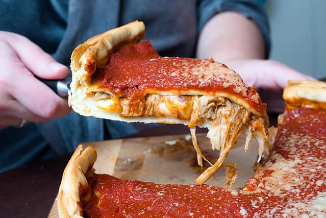 Top view of Chicago pizza. Woman hands cutting Chicago style deep dish italian cheese pizza with tomato sauce and beef meet inside