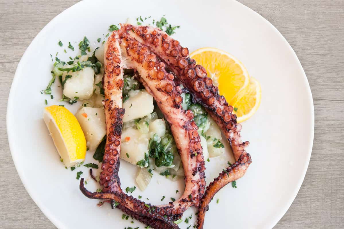 Grilled octopus with potato and lemon on plate top view