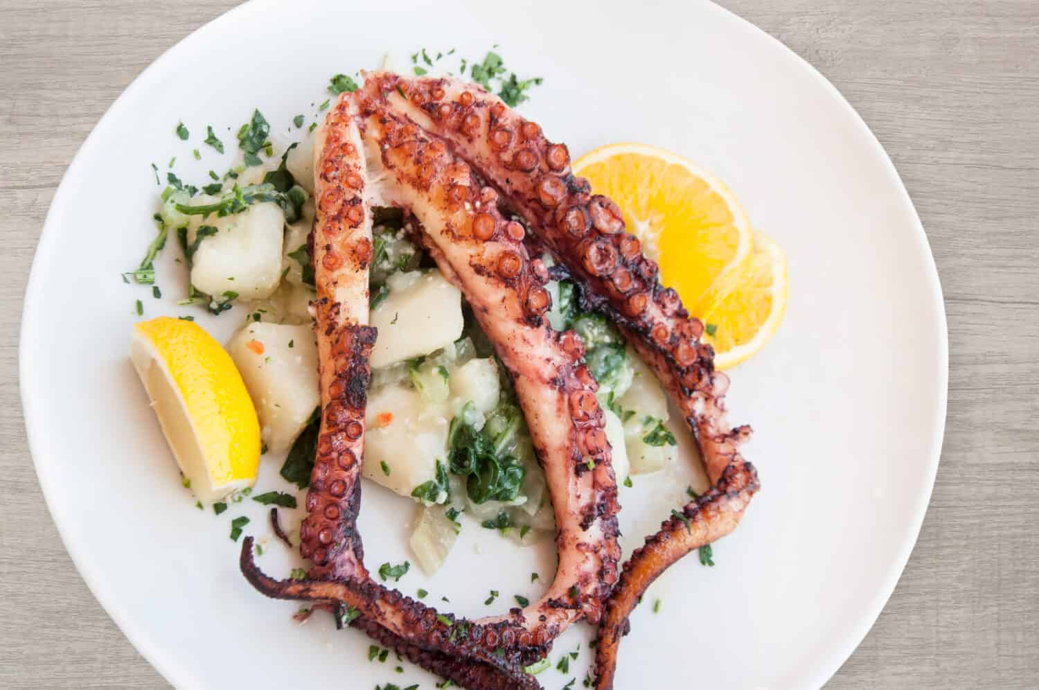 Grilled octopus with potato and lemon on plate top view