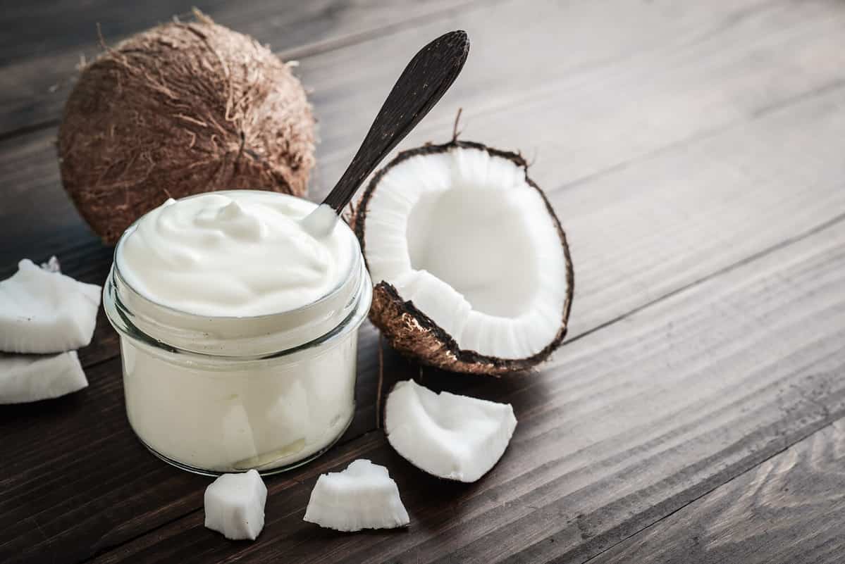 Coconut cream in a glass jar with fresh coconut on a wooden background. Healthy vegan food concept.