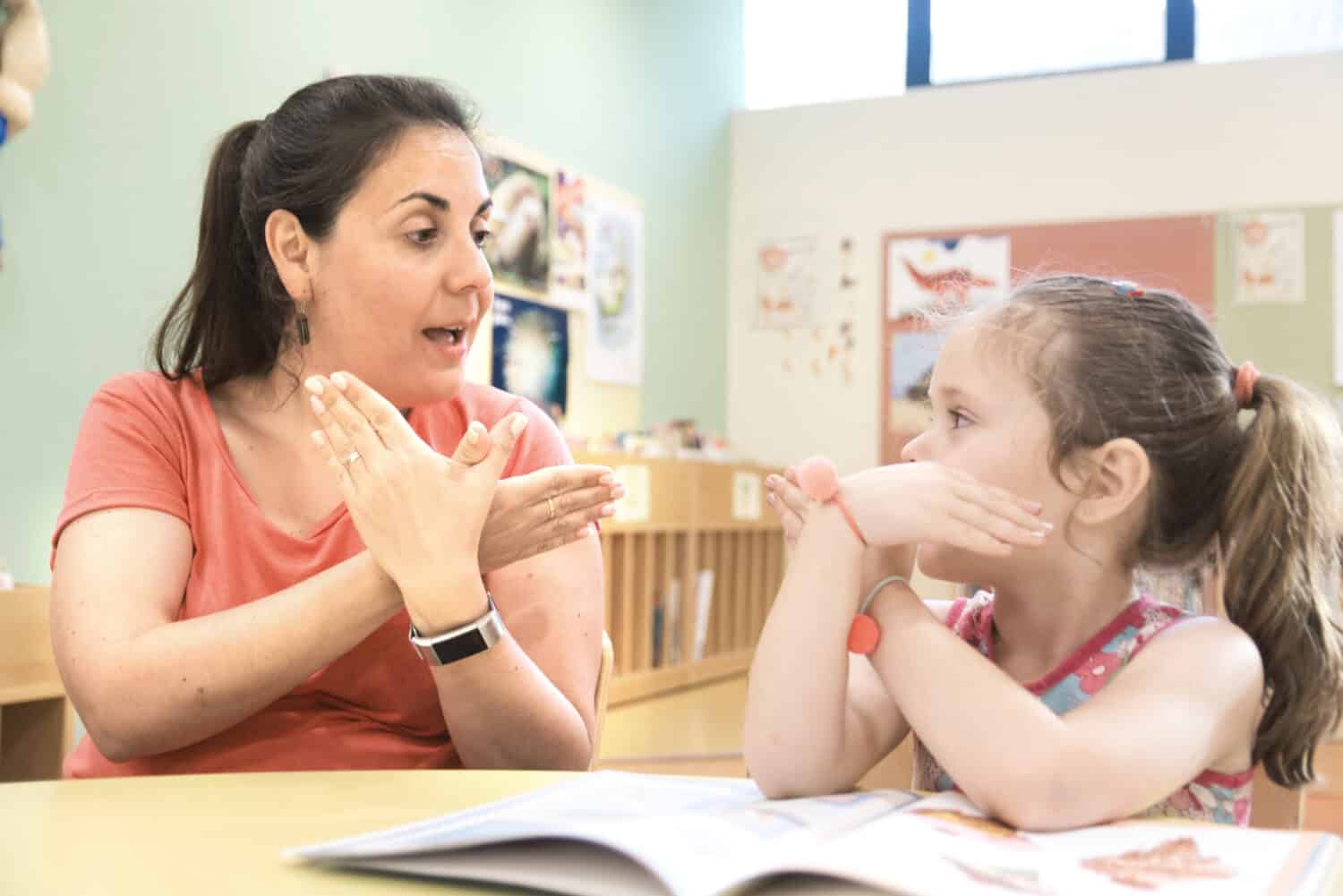 Sign language teacher in a extra tutoring class with a deaf child girl using American Sign Language.