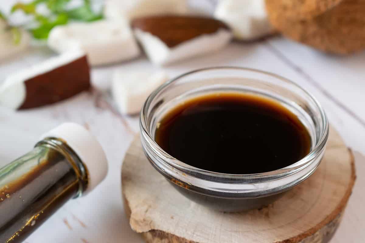 Coconut Aminos in a small glass bowl on a white wooden table. Soy sauce substitute. Light background