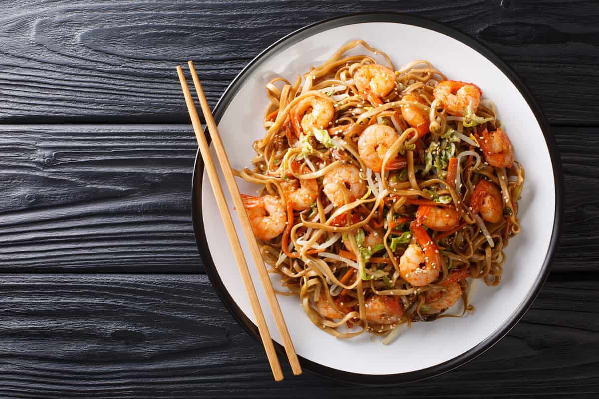Authentic chow mein noodle fried with shrimp, vegetables and sesame seeds close-up on a plate on the table. Horizontal top view from above