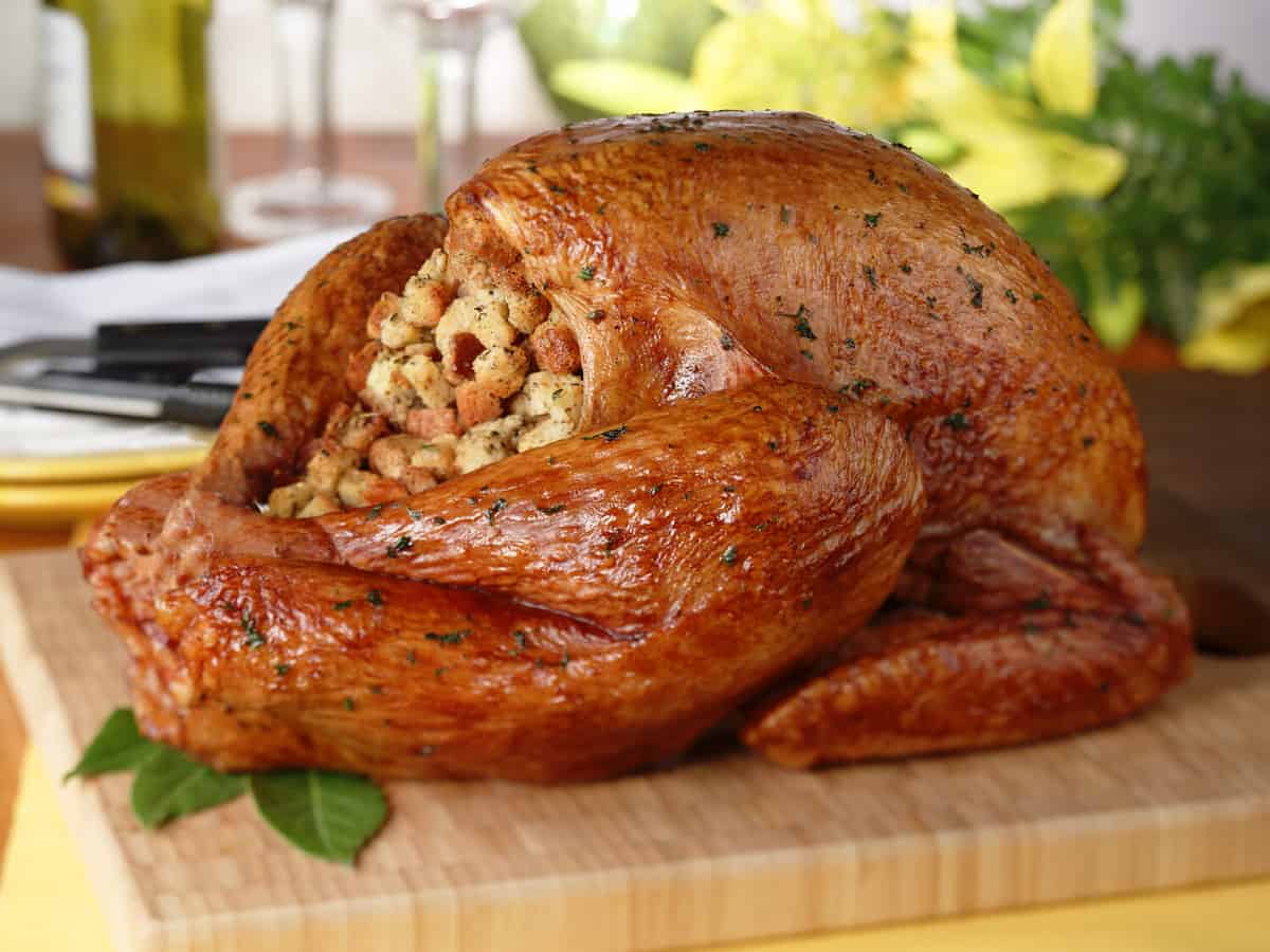 Whole roast turkey with stuffing on wood cutting board.