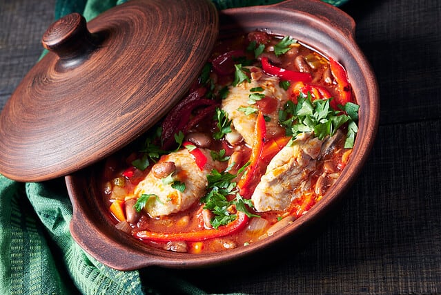 Healthy chicken stew of chicken breasts stewed in tomato sauce with vegetables and red kidney beans served on a rustic clay pot on a dark wooden background, top view, horizontal orientation