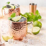 Cold Moscow Mules cocktail with ginger beer, vodka, lime. White stone background.