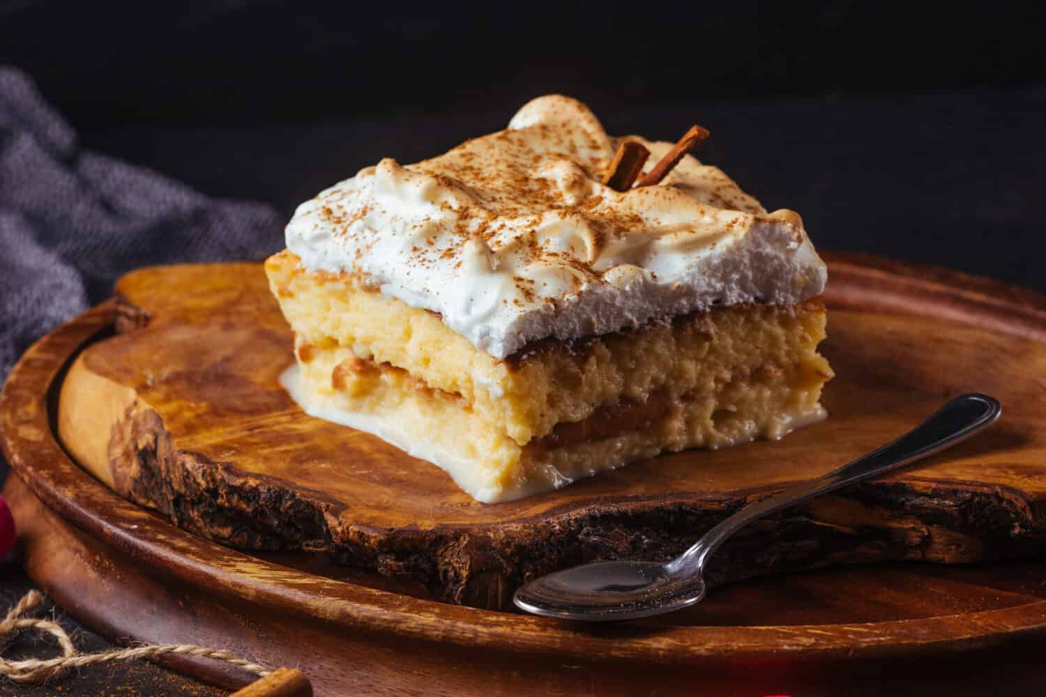 Piece of cake three milk prepared at home. The image is made on a dark background and rustic boards. Latin American dessert