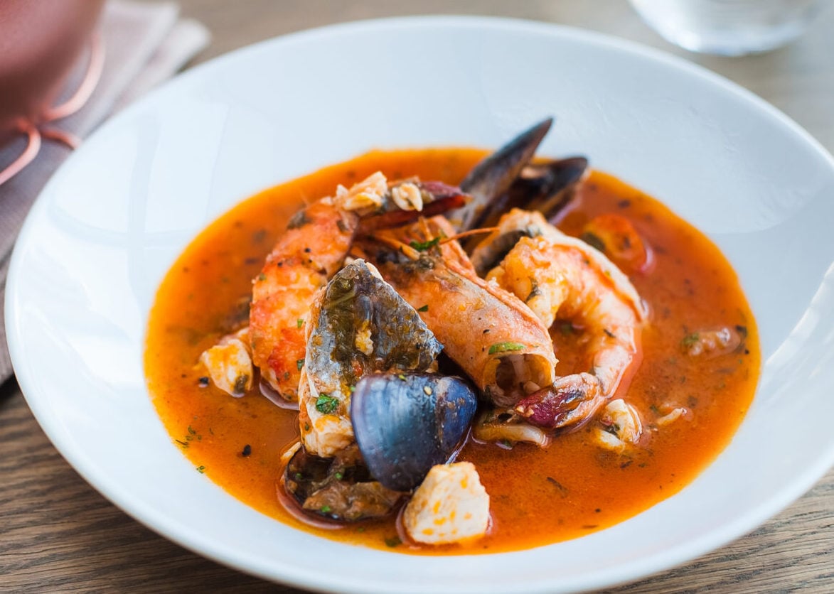 Bouillabaisse soup with shrimps, mussels and fish in a white plate on a wooden table