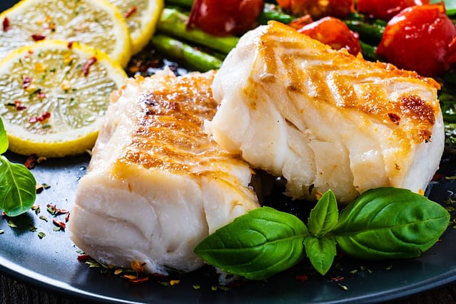 Fish dish - fried cod fillet with asparagus on wooden table