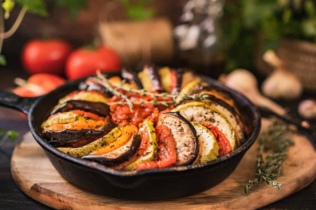 Ratatouille made of zucchini, eggplants, peppers, onions, garlic and tomatoes slices with aromatic herbs. Rustic wooden table. Traditional French food, vegetable, vegan healthy dish. Copy space