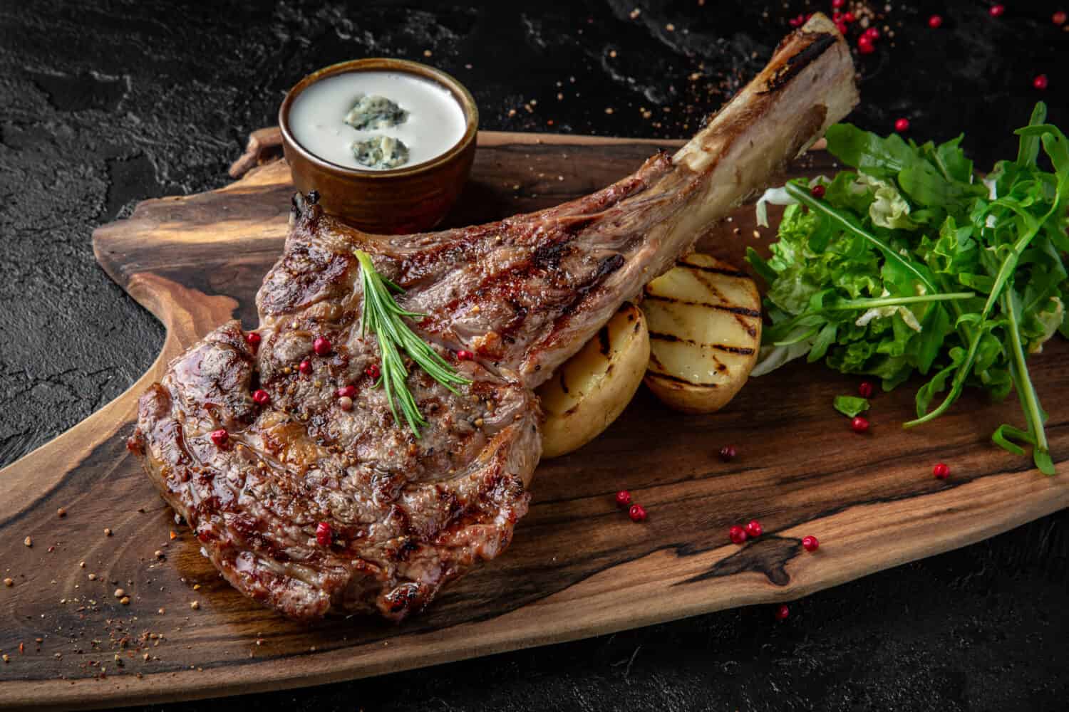 Juicy delicious ribeye or tomahawk steak on the bone with baked potatoes, spices and herbs. Hearty meat dish