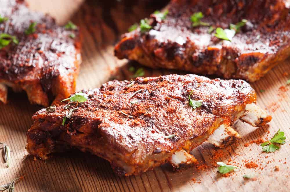 Close up of a portion of barbecued grilled ribs seasoned with hot spices and fresh herbs on a wooden board