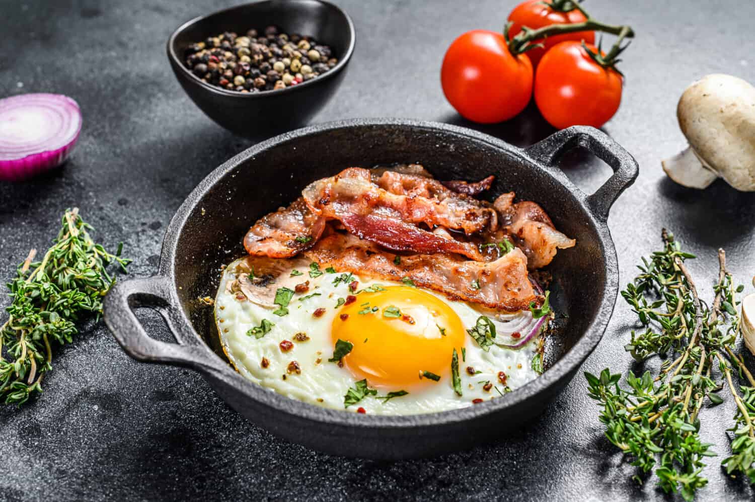 English breakfast, fried egg, tomatoes, mushrooms, bacon. Black background. Top view