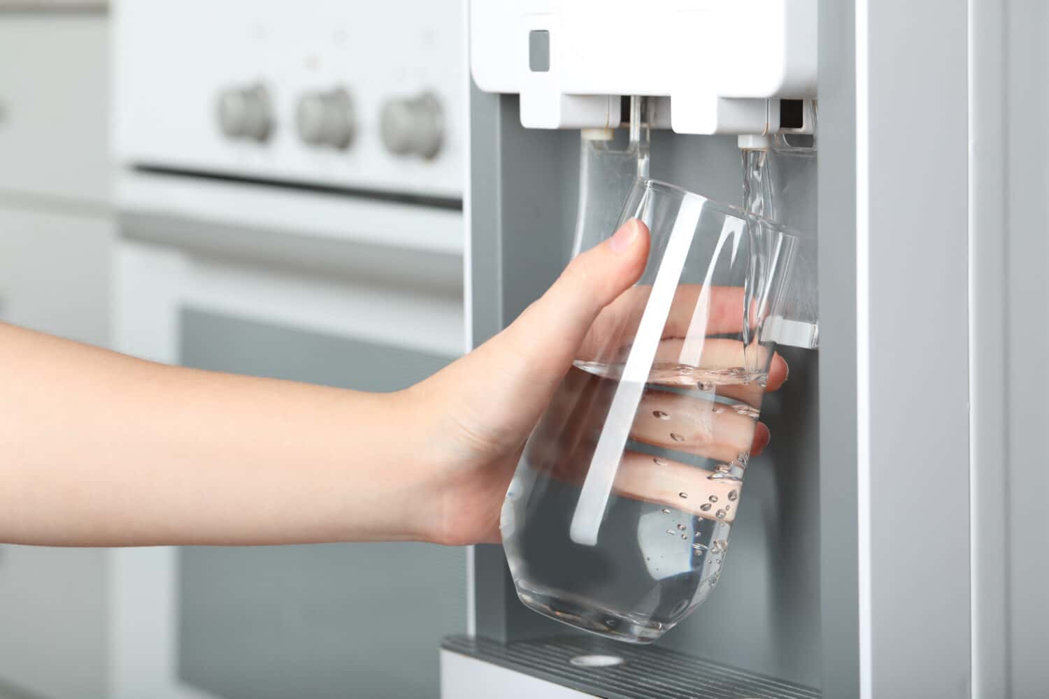 Woman filling glass with water cooler indoors, closeup. Refreshing drink