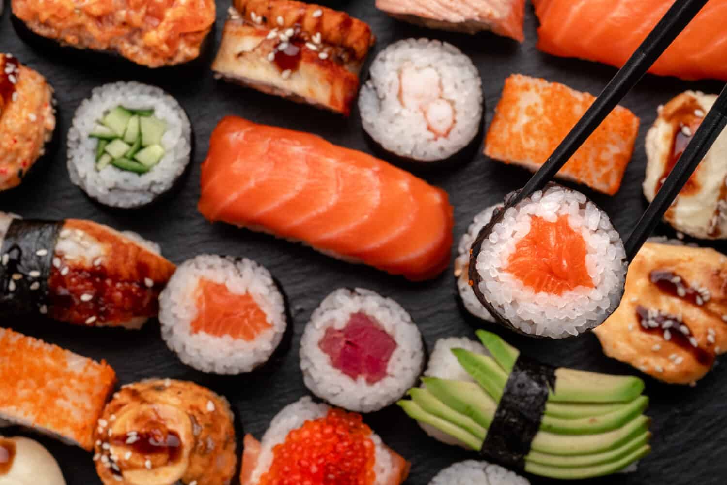 Assorted sushi nigiri and maki big set on slate. A variety of Japanese food with tuna, crab, salmon, eel and rolls. Take sushi in chopsticks