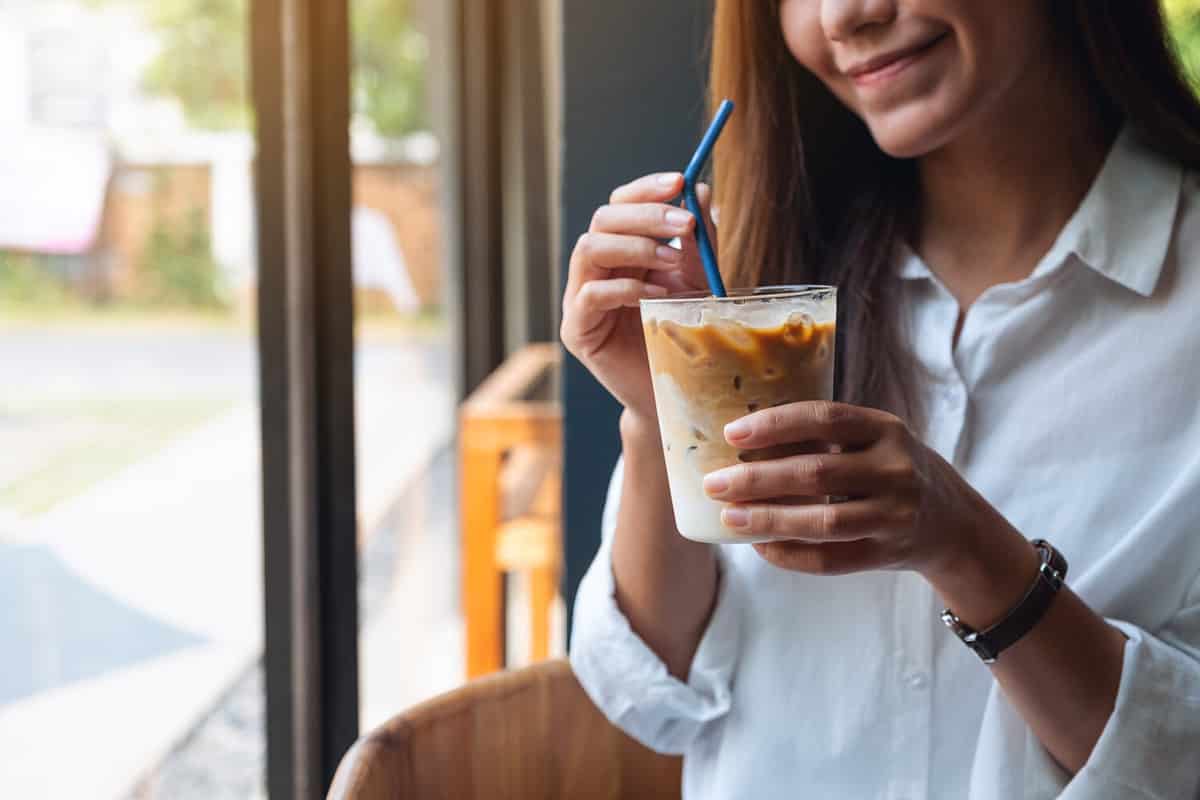 Closeup image of a beautiful young asian woman holding and drinking iced coffee