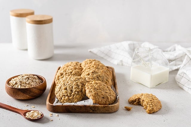 Homemade oatmeal cookies with banana, oats and nuts on a wooden tray and a cup of milk. Side view, copy space for text. Healthy food. Oatmeat biscuits. Horizontal