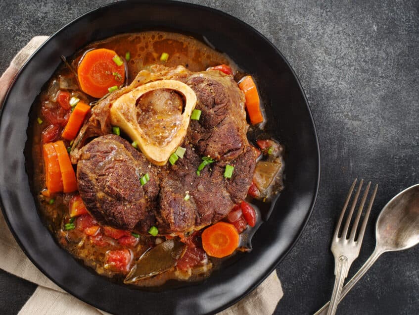 Italian menu: braised veal steak Ossobuco alla Milanese with vegetable sauce close-up. Beef Leg Slice with marrow. Top view, flat lay.