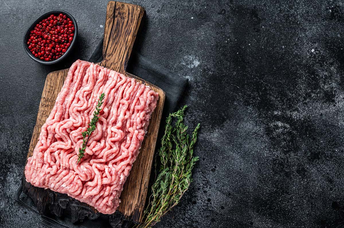 Ground chicken or turkey raw meat on wooden board. Black background. Top View. Copy space