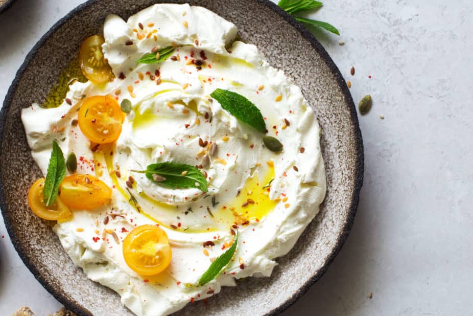 Homemade yogurt cheese (labneh) with tomatoes, seeds and oive oil in rustic plate on gray stonebacground close up. Flat lay