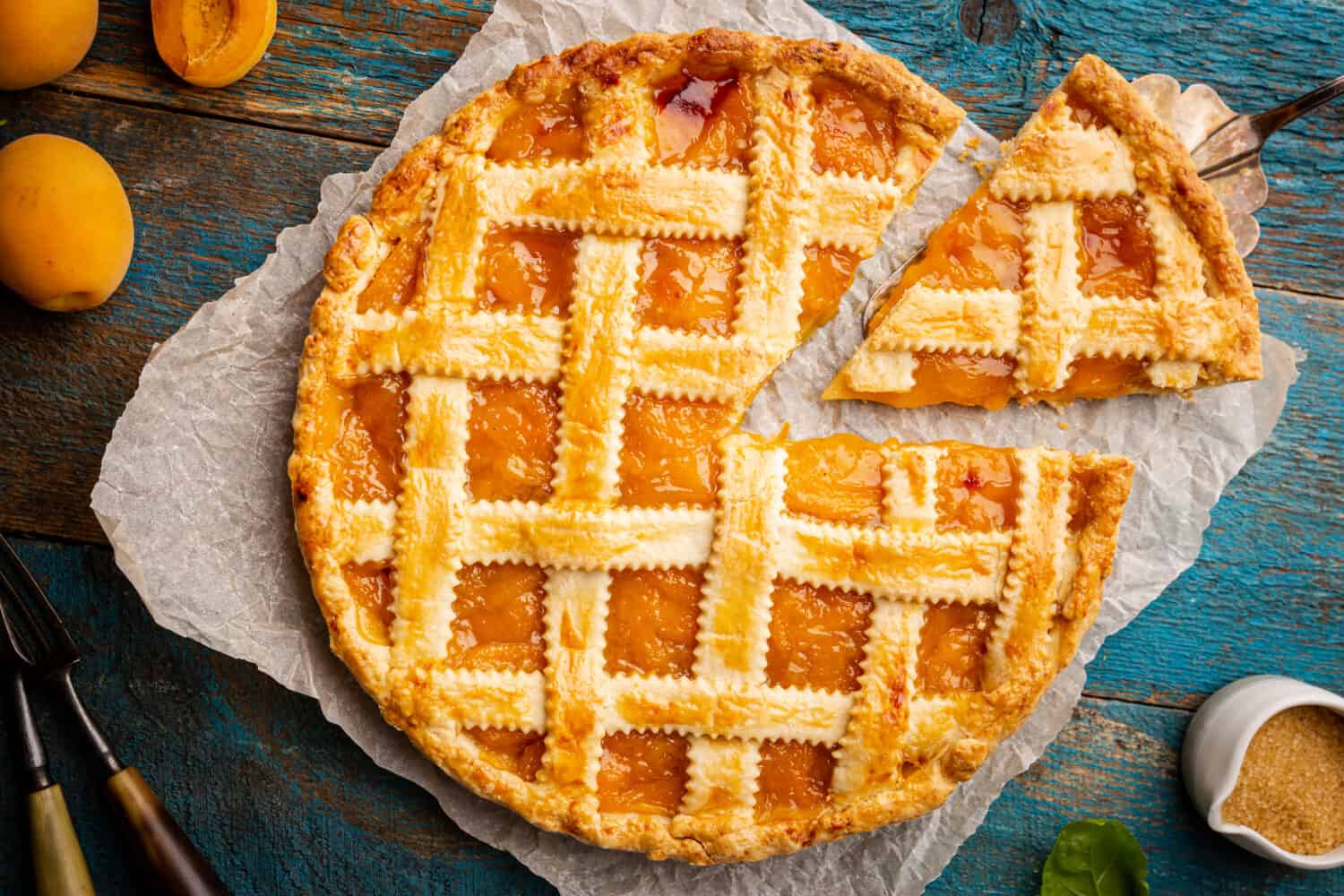 Summer apricot or peach pie homemade on blue wooden background, top view. Delicious fruit dessert. Fruit cake. Copy space.