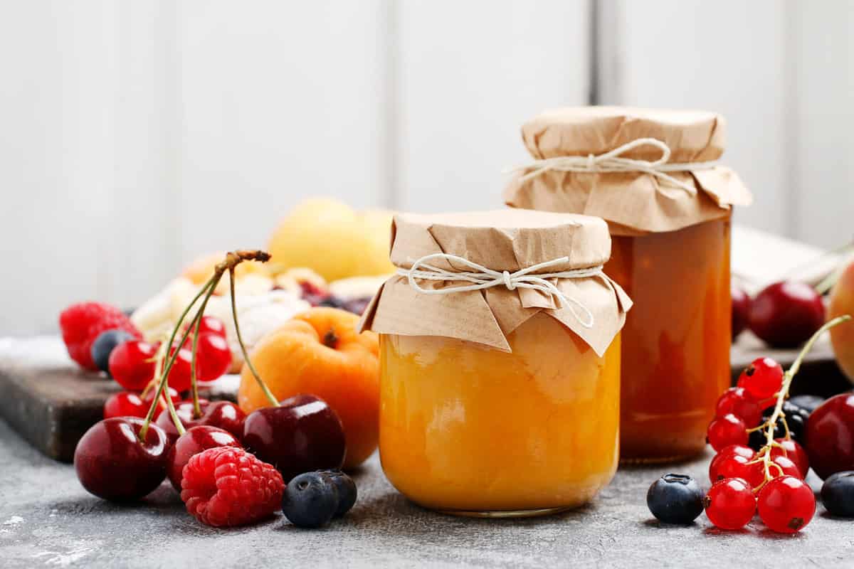 Two jars with peach jam and fresh fruits on stone background.