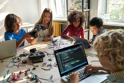 Diverse school children students build robotic cars using computers and coding. Happy multiethnic kids learning programming robot vehicles sitting at table at STEM education science engineering class.