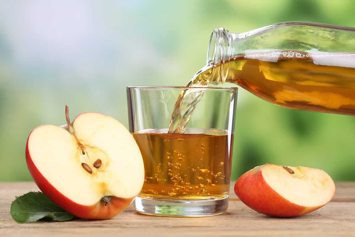 Apple juice pouring from red apples fruits in summer into a glass