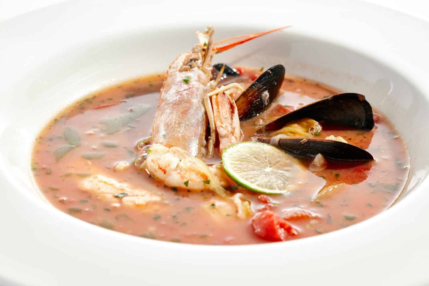 Tomato seafood soup in plate isolated on white background. Seafood stew Cioppino - shrimp,  mussels and salmon in tomato broth. Seafood dish in Italian restaurant menu