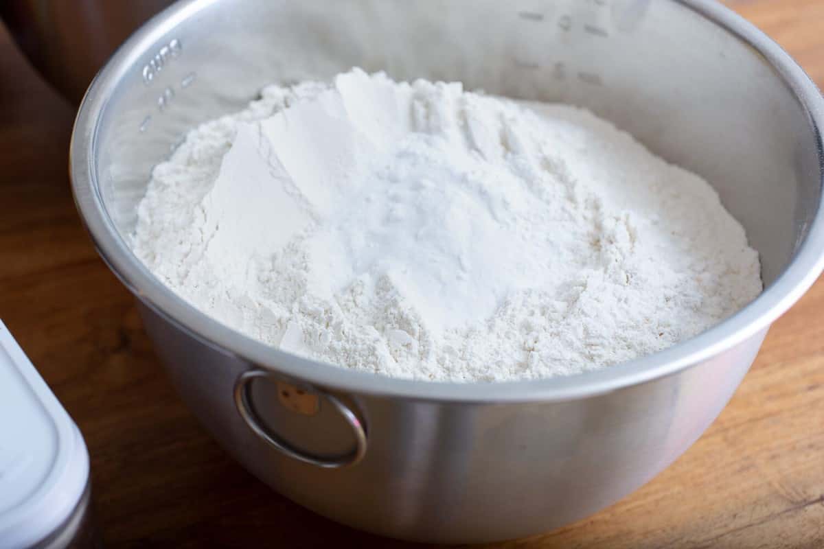 A view of a large bowl of flour on a wood table.