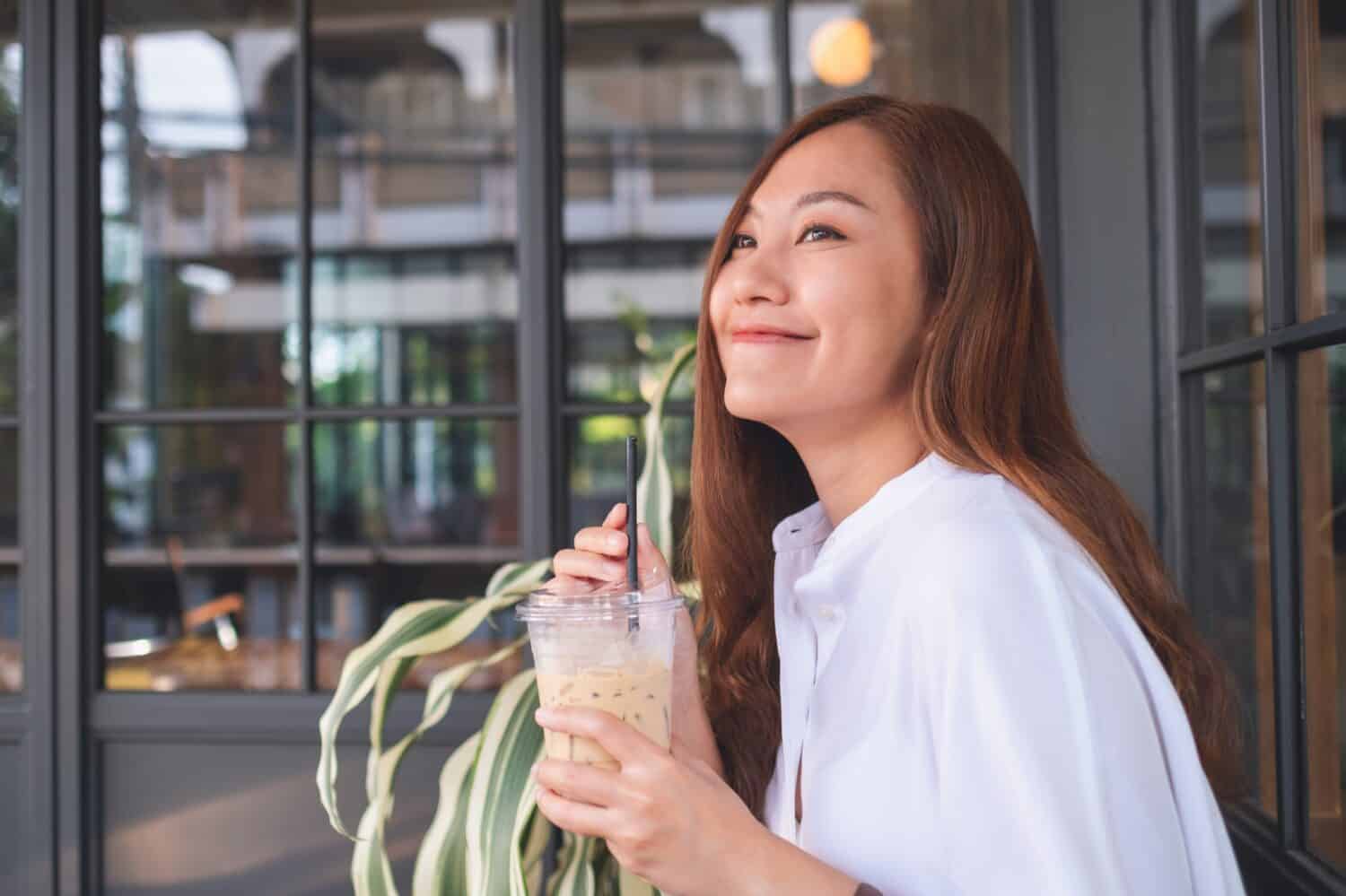 Portrait image of a beautiful young asian woman holding and drinking iced coffee
