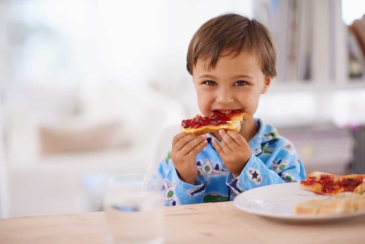 Nothing beats a good breakfast. A cute little boy eating toast with jam.