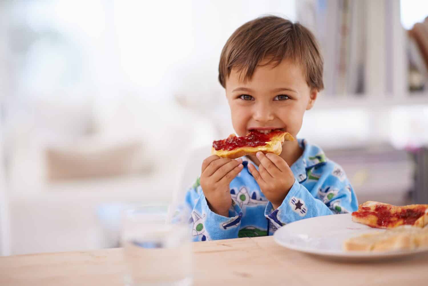 Nothing beats a good breakfast. A cute little boy eating toast with jam.