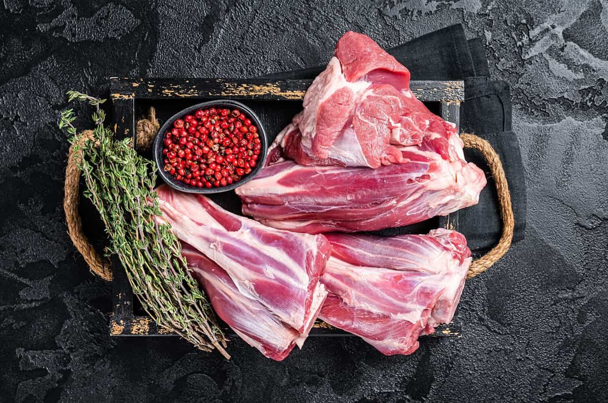 Fresh Raw lamb shanks with herbs and spices, mutton meat. Black background. Top view.