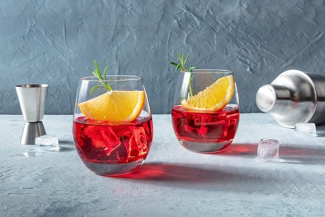 Campari or negroni cocktail with fresh orange slices, a jigger and a shaker, with rosemary for garnish. A summer cocktail. With copy space