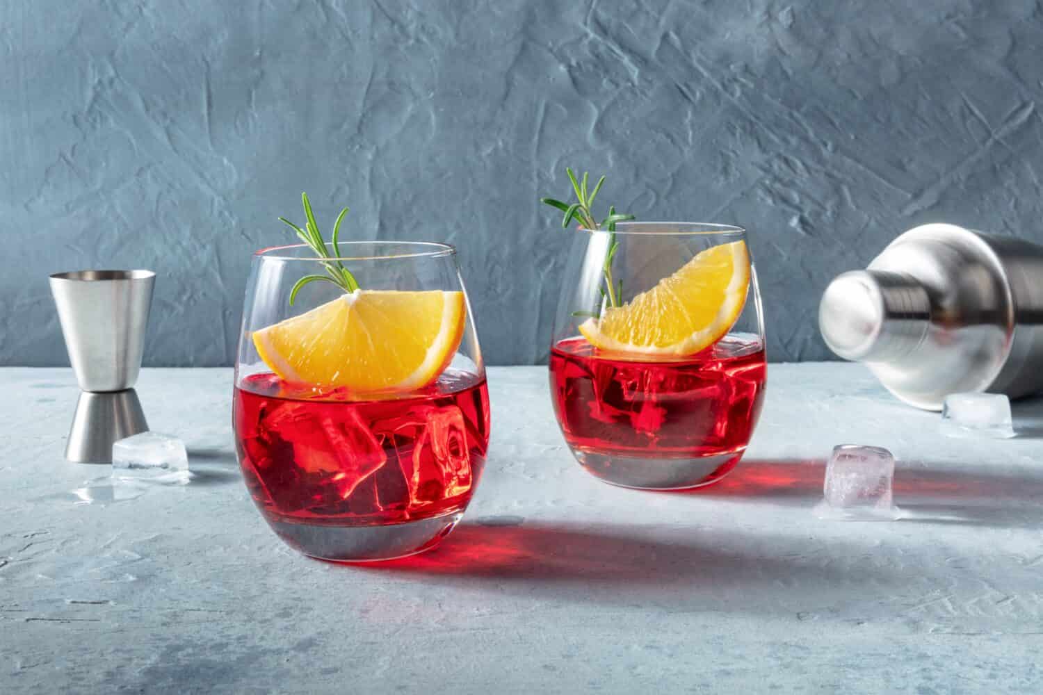 Campari or negroni cocktail with fresh orange slices, a jigger and a shaker, with rosemary for garnish. A summer cocktail. With copy space