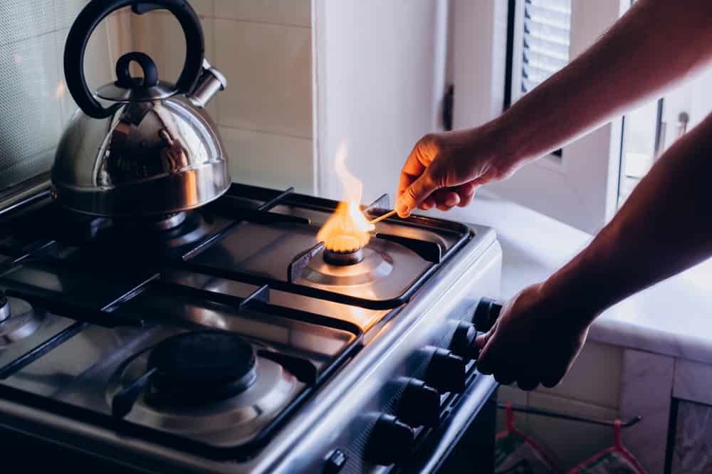 A man's hand with a match lights a gas burner or a gas stove in the kitchen.